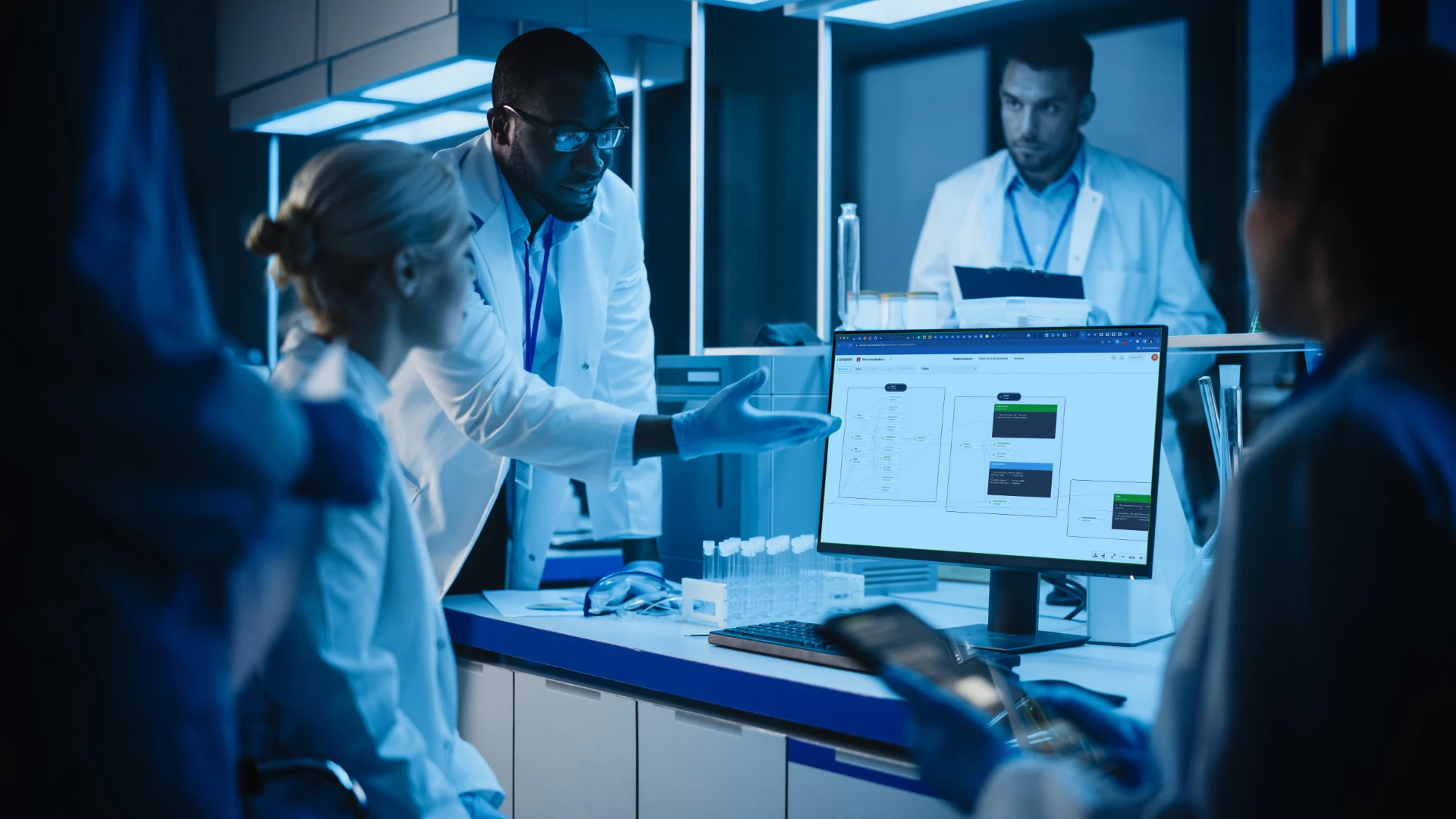 Scientists in lab coats discussing data displayed on a computer monitor in a laboratory.